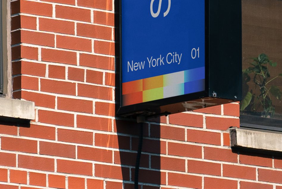Blue digital display screen on red brick building with rainbow color bar at bottom