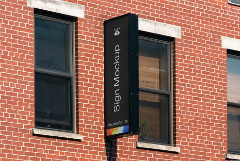 Vertical black pole sign on brick storefront with rainbow accent strip at base