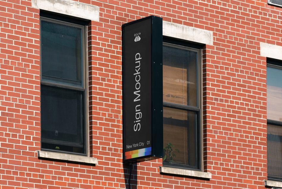 Vertical black pole sign on brick storefront with rainbow accent strip at base