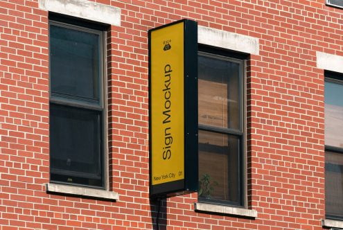Yellow vertical pole sign on red brick wall between two dark window frames