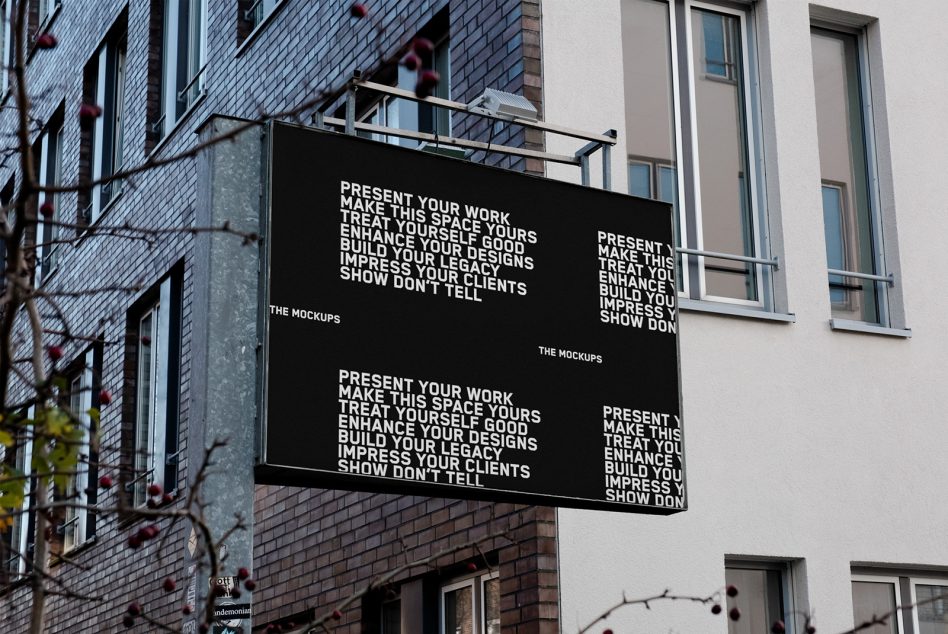 Black wall-mounted billboard mockup on brick facade between modern buildings with vines