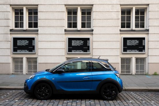 Blue compact car parked in front of building with window mockups displaying text for urban graphic design advertisement.