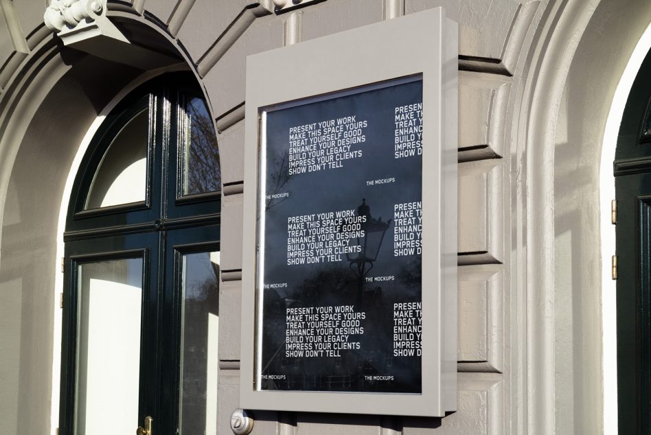 Dark framed poster mockup on white building exterior near decorative archway