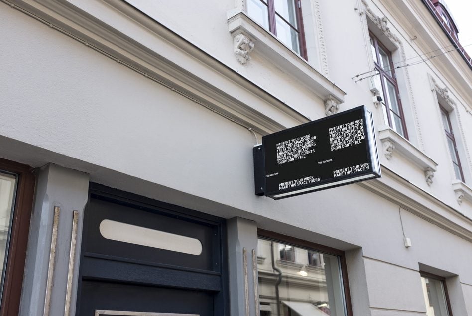 Black horizontal sign with white text mounted on light building facade above glass door