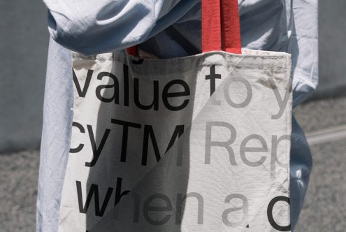 Cotton tote bag with black typography overlaid on cream fabric, red ribbon handle