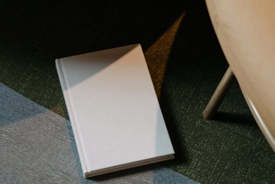 Closed blank book mockup on a green patterned carpet with shadows, ideal for graphic design and cover presentations.