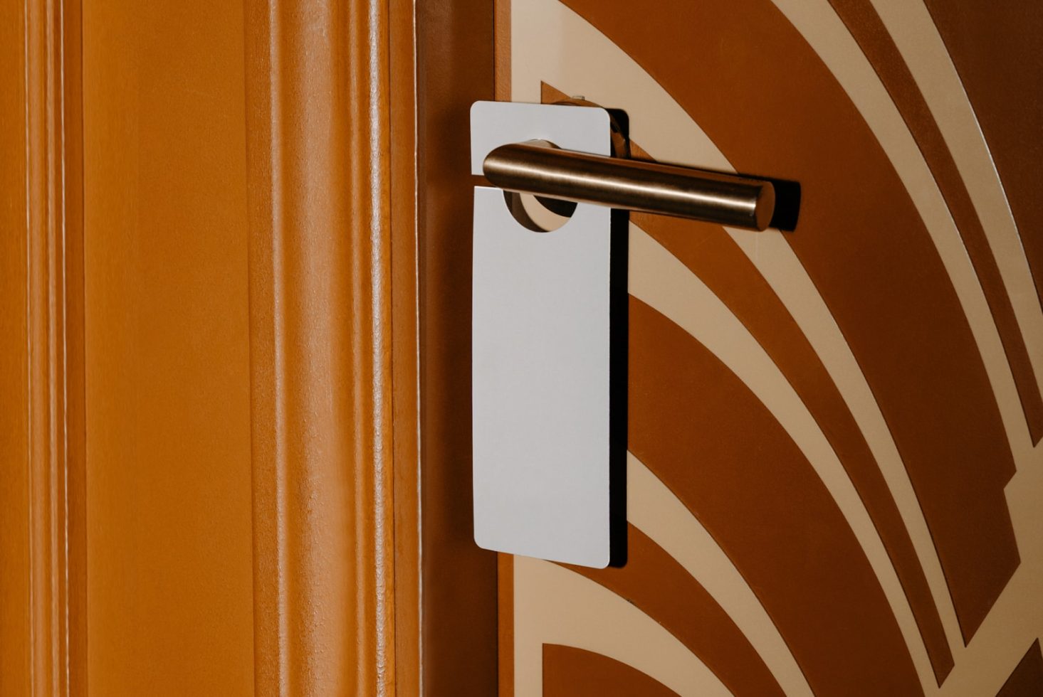 Blank white door hanger mockup on a brown hotel door with a geometric pattern, elegant presentation for branding designs.