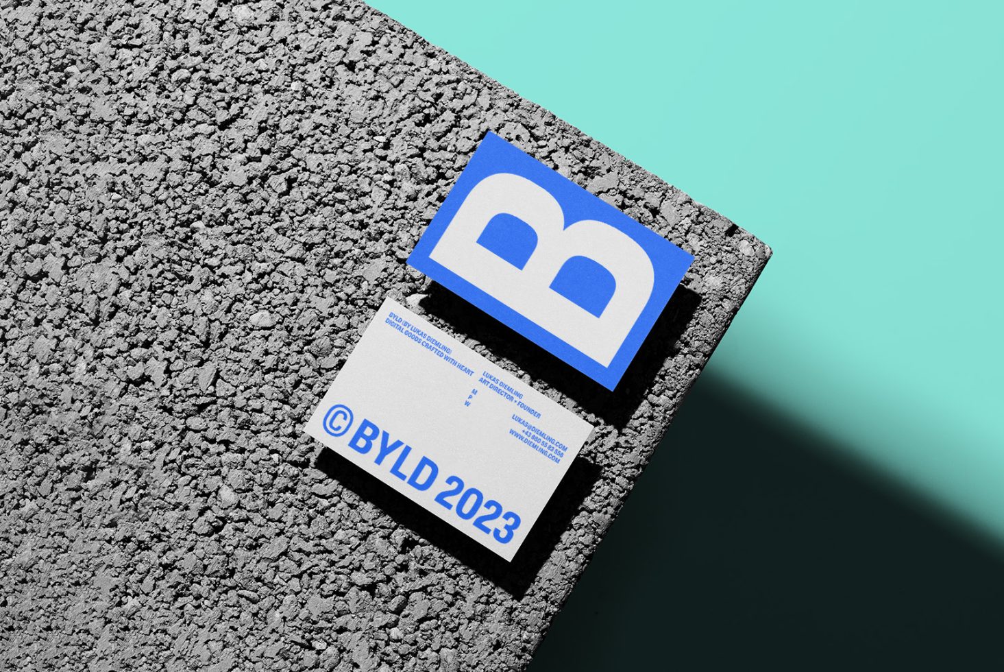 Business card mockup with textured overlay, blue and white design elements, resting on a rough surface with a teal background.