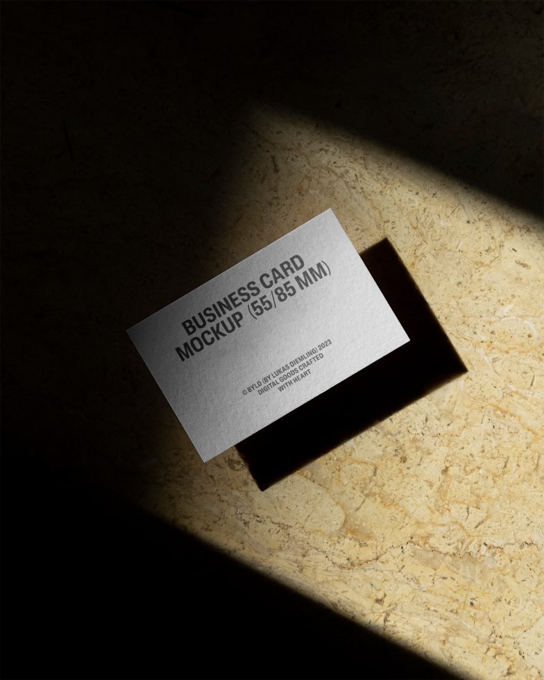 Elegant business card mockup on textured surface with dramatic lighting, perfect for designers looking to showcase brand identity in a realistic setting.