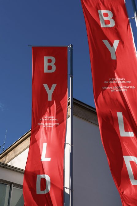 Three red vertical banners with bold white text on building exterior, clear blue sky background, graphic design mockup.