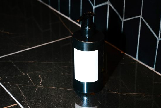 Black dispenser bottle mockup with blank label on dark tiled background, ideal for branding and packaging design presentations.