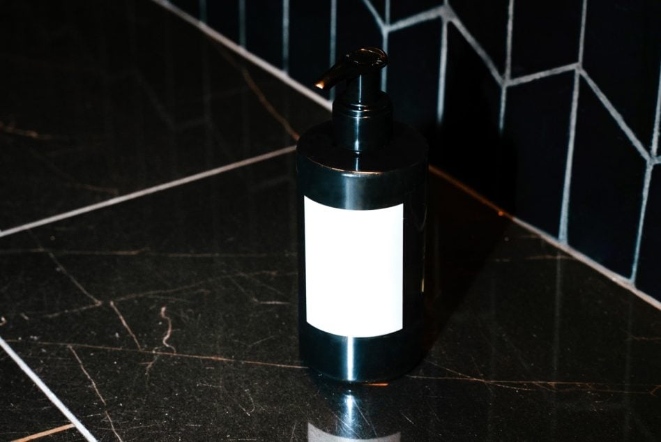 Black hand soap pump with blank label on dark marble counter against geometric tile wall