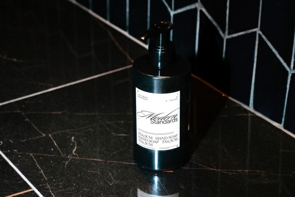 Dark soap dispenser with printed label sitting on black marble surface with geometric tile backdrop