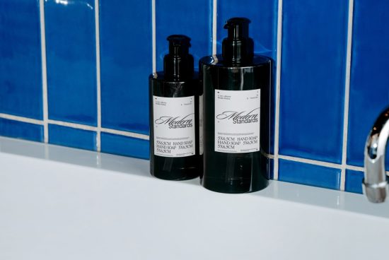 Two black hand soap bottles with elegant labels on white sink against blue tile background, suitable for mockup designs.