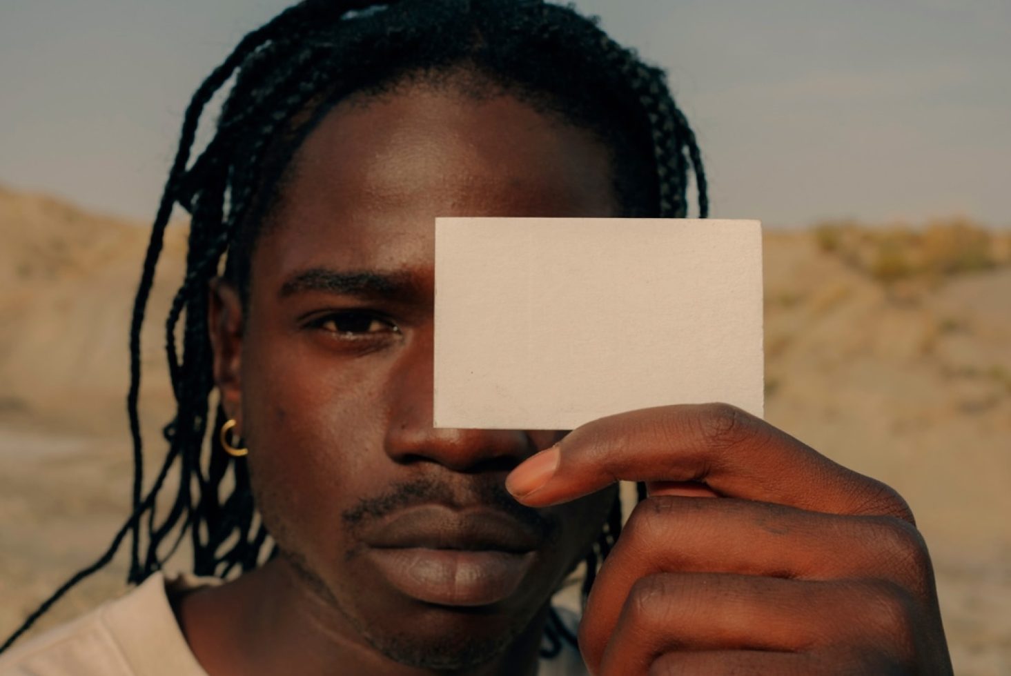 Man holding a blank business card mockup in front of his face, ideal for branding designs with a personal touch in natural light.