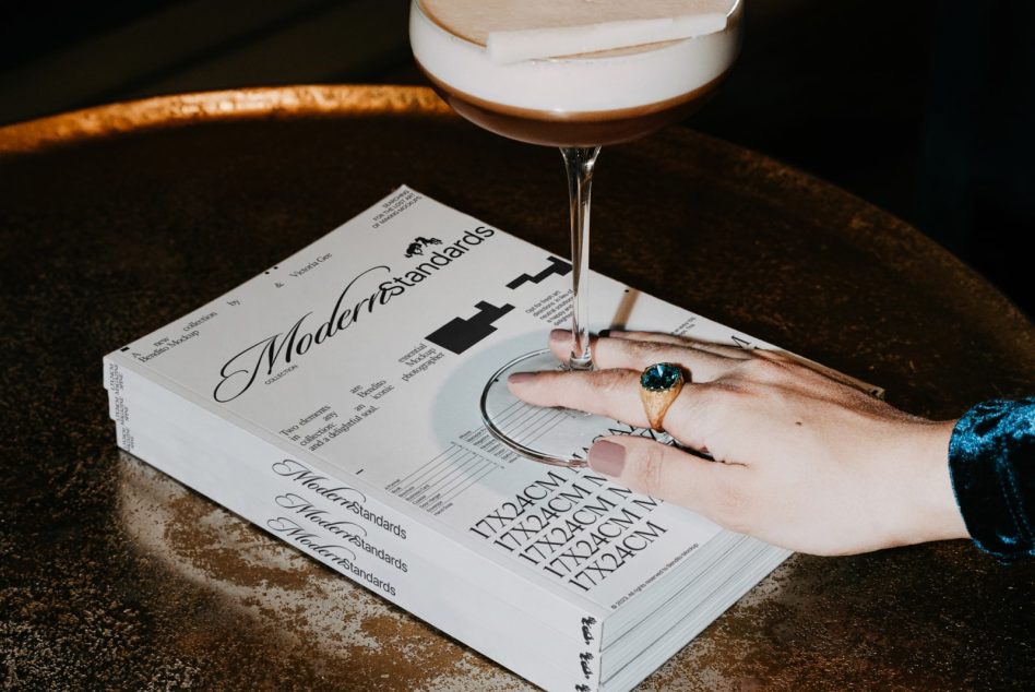 Hand holding magazine with rings, cocktail glass, copper tray, styled scene