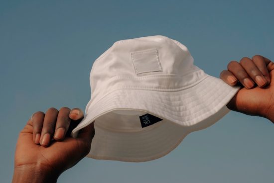 Hands holding a white bucket hat against a blue sky, fashion accessory mockup, minimalist design, clear space for branding