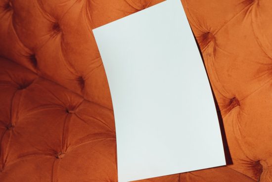 Blank white paper on an orange velvet textured sofa for mockup display, graphic design templates and presentations.