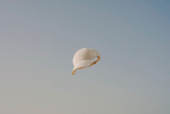 White baseball cap floating against a clear blue sky, minimalistic design, ideal for mockup graphics and advertising templates.