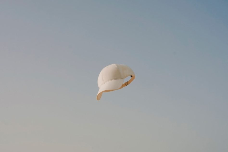 Blank white baseball cap floating isolated on soft gradient sky background