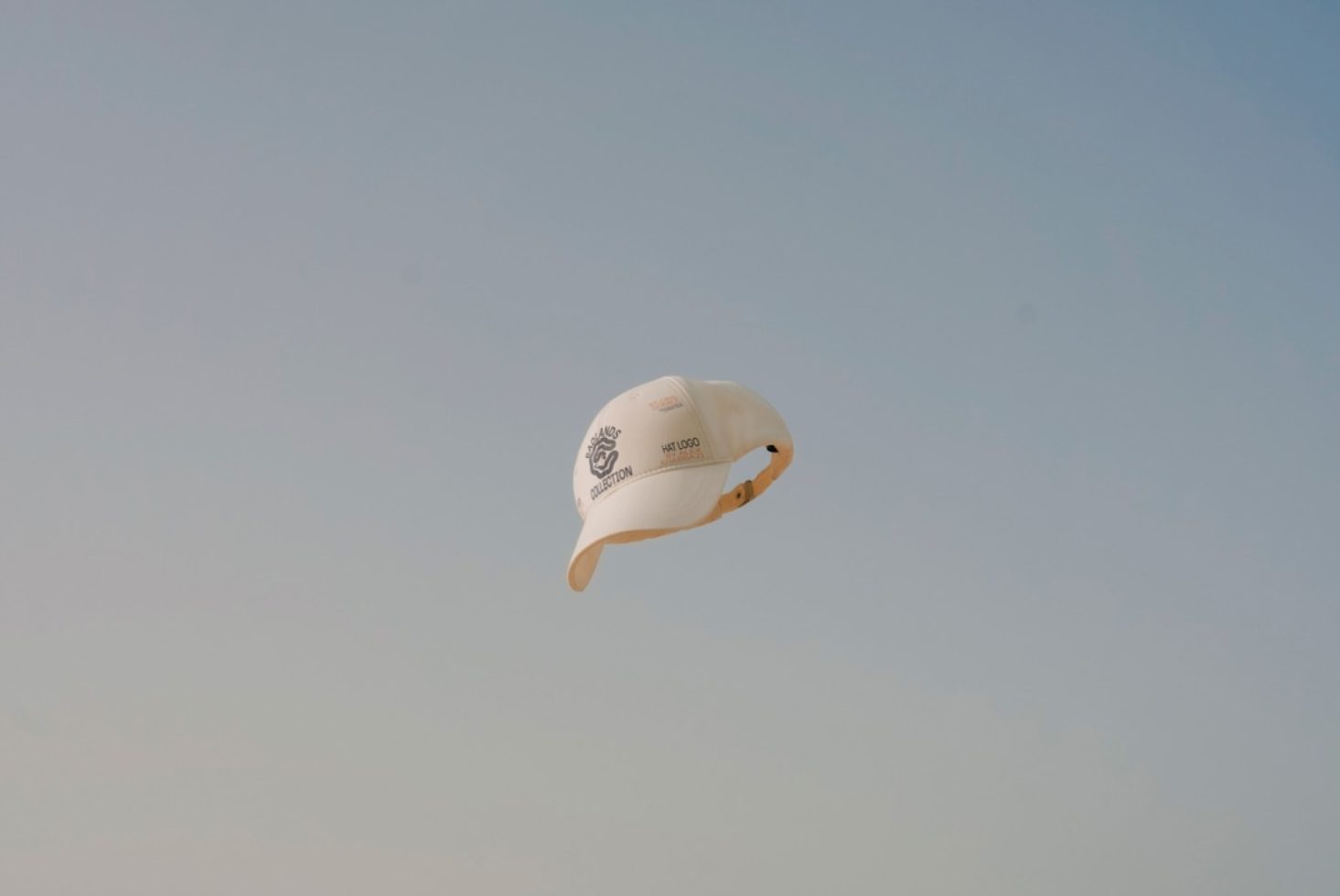 Floating white baseball cap mockup against a clear blue sky, suitable for showcasing logo and design projects for apparel and fashion accessories.