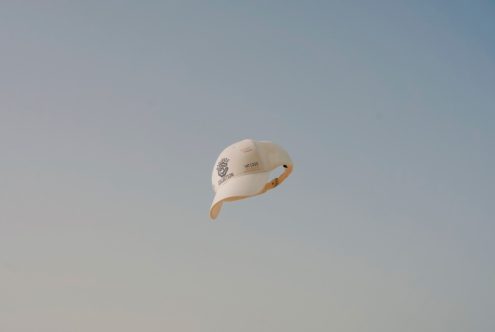 Floating white baseball cap mockup against a clear blue sky, suitable for showcasing logo and design projects for apparel and fashion accessories.