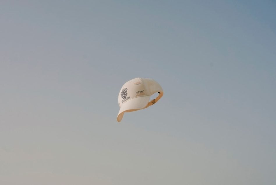 Floating cream cap with tan strap shown against clear blue sky backdrop