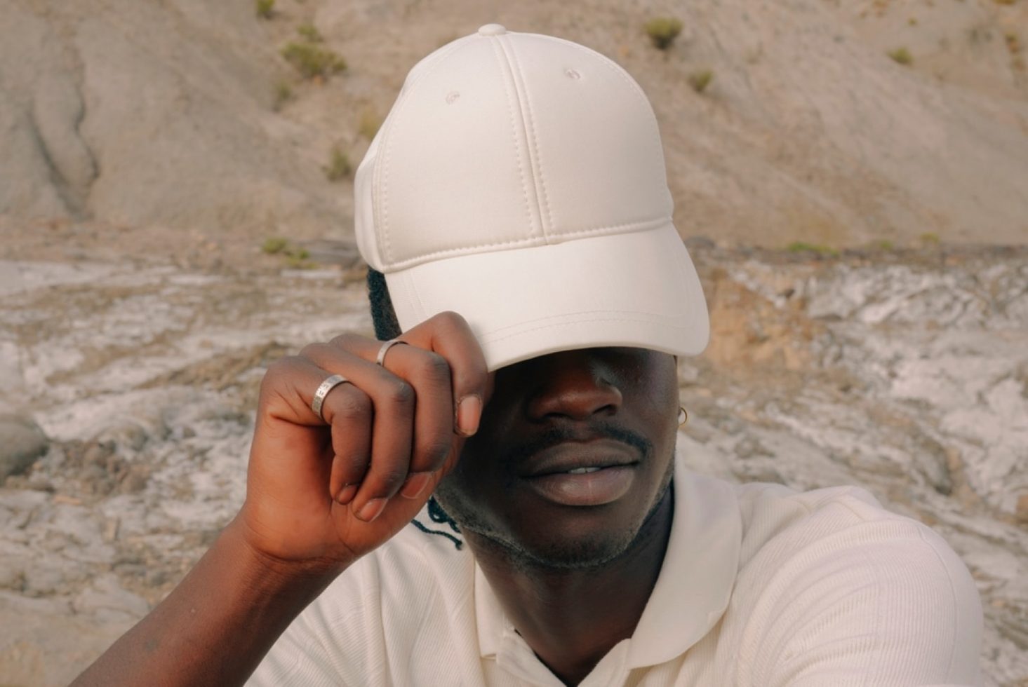 Stylish man in white cap and polo for fashion mockups, outdoor portrait, serene expression, casual attire, design asset.