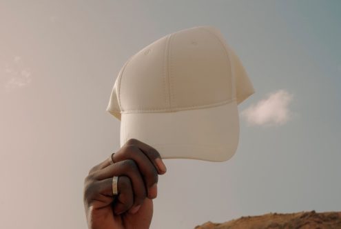 Person holding a blank white baseball cap mockup against sky, ideal for branding designs and logo presentation.