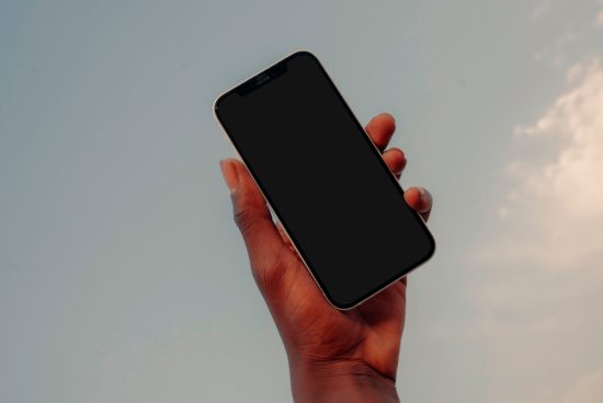 Hand holding smartphone with blank screen on sky background, ideal for mockup designs, app presentation, digital asset.