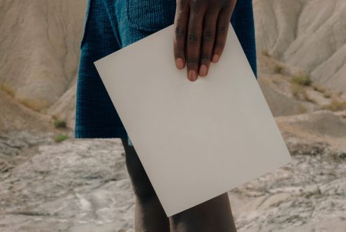 Person holding blank white paper mockup in a natural outdoor setting, ideal for showcasing design work and graphic presentations.