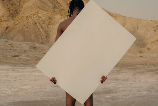 Person holding a blank poster mockup in a desert setting, ideal for showcasing graphic designs and typography.