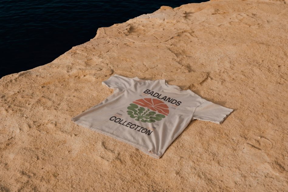 Graphic t-shirt mockup on a sandy cliff with ocean background, natural lighting, realistic texture, perfect for apparel design presentations.