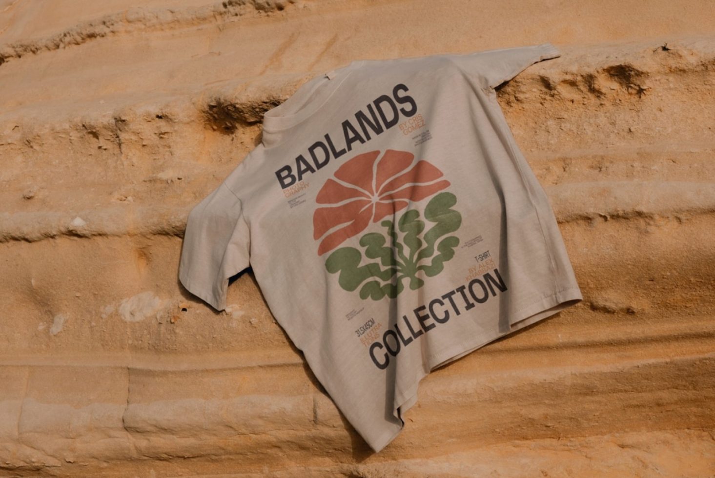 Gray T-shirt mockup with natural Badlands motif design laid on sandy rock texture, perfect for apparel presentation and graphic display.