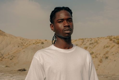 Young man in white t-shirt posing with serene expression in desert landscape, ideal for apparel mockups and fashion design templates.