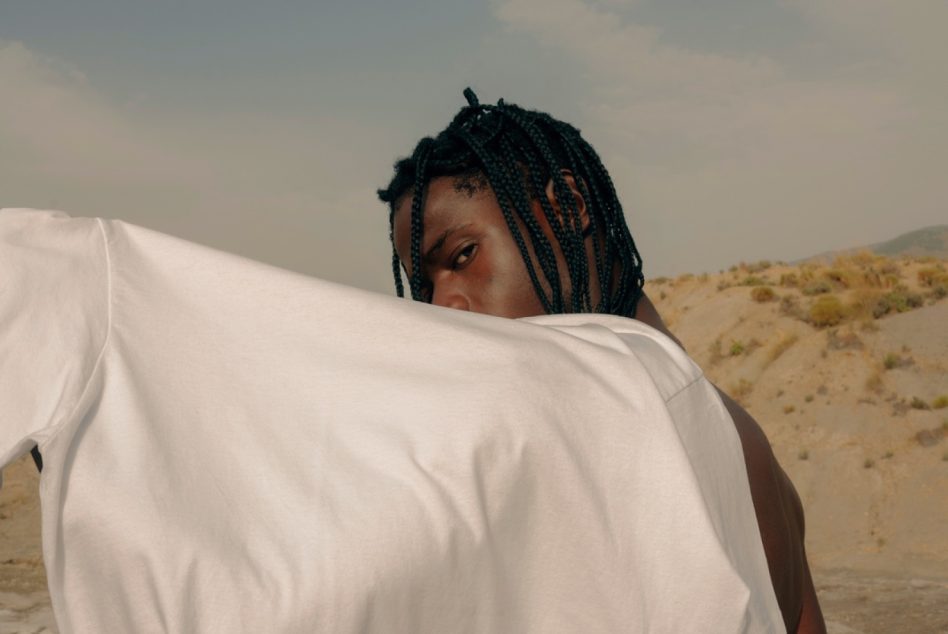 Man with braids wearing a white t-shirt posing in desert setting, suitable for fashion mockups, diverse model photography, and apparel design.