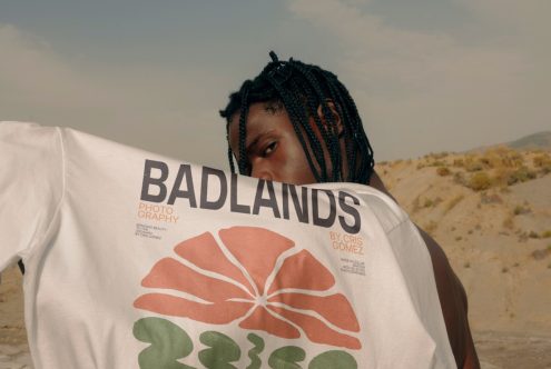 Man with braided hair showcasing a graphic t-shirt with BADLANDS print, outdoor setting for stylish apparel mockup.