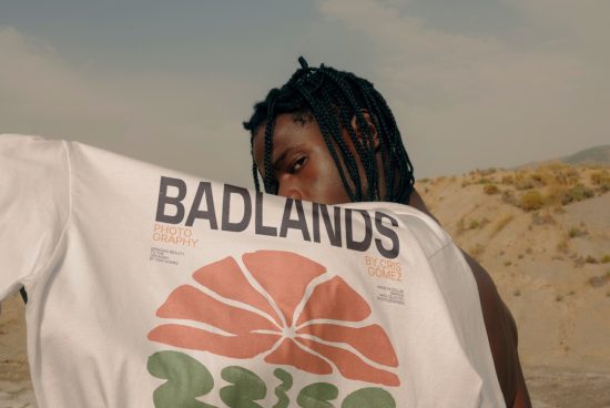 Man with braided hair showcasing a graphic t-shirt with BADLANDS print, outdoor setting for stylish apparel mockup.