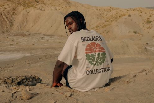 Man in graphic tee sitting in arid landscape, back view, designer apparel mockup, natural earthy tones, outdoor photoshoot, fashion graphic print.