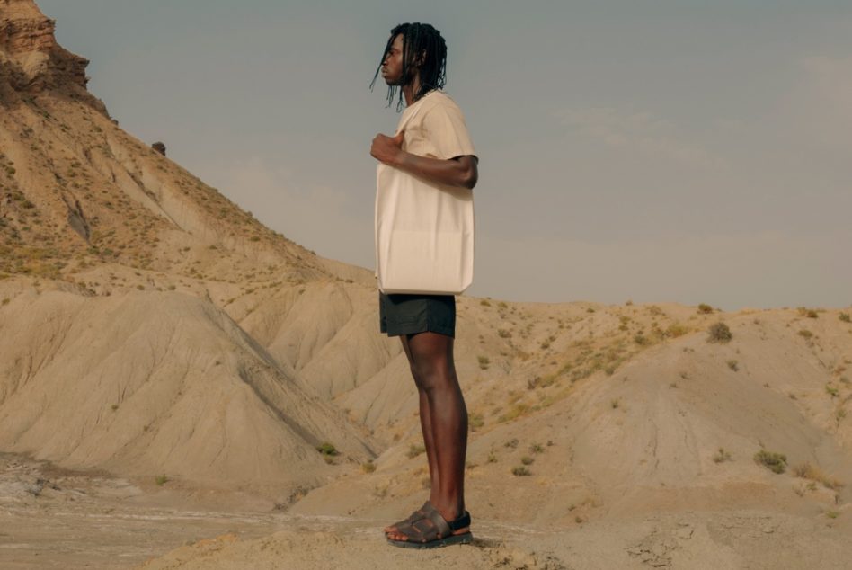 Back view of cream oversized t-shirt on model in sandy terrain
