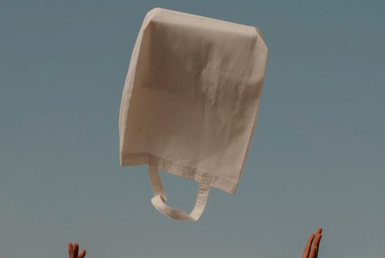 Floating tote bag mockup with hands reaching out against clear blue sky, ideal for eco-friendly shopping bag designs.