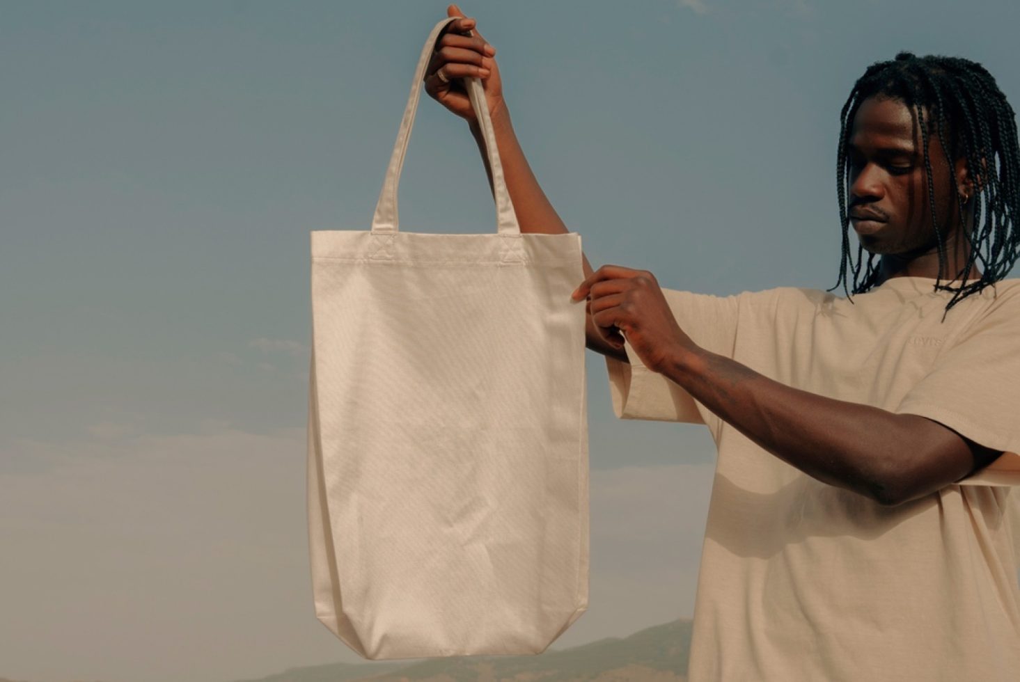 Man holding blank white tote bag mockup in natural light, ideal for eco-friendly bag design presentations.