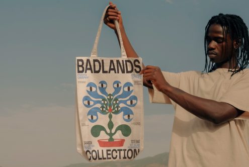 Man holding tote bag with graphic design mockup, clear sky background, potential for eco-friendly product branding.