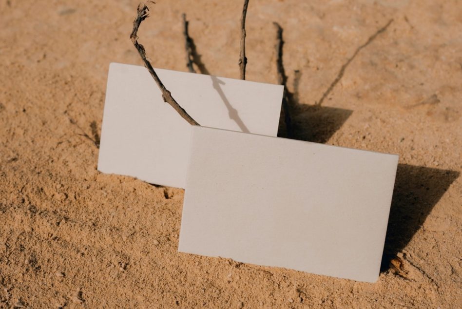 Blank folded business cards nestled between twigs in desert sand