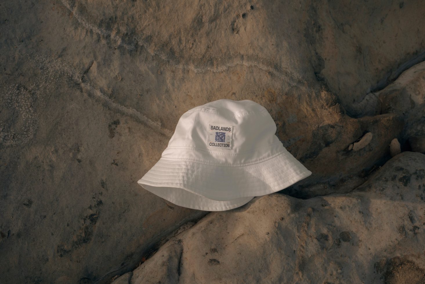 White bucket hat with logo mockup on a rocky surface, perfect for branding presentations and headwear design showcase.