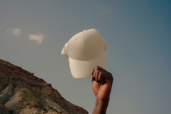 White baseball cap mockup held against a sky backdrop with a hand, suitable for logo and design placement. Perfect for apparel mockups and fashion projects.