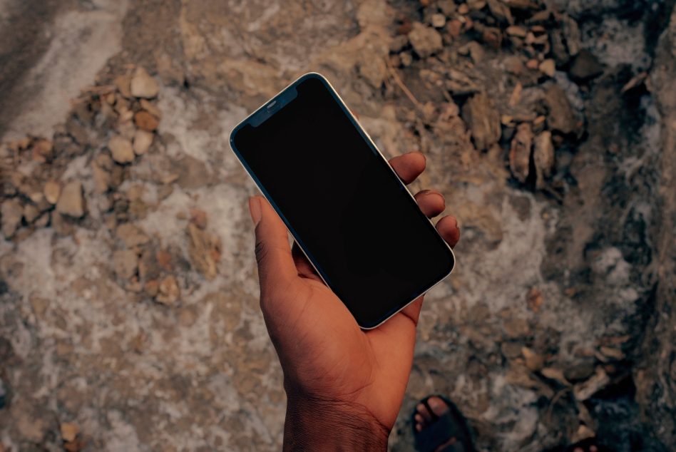 Blue iPhone with black screen held in hand over textured rocky ground