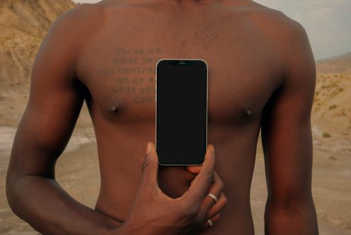 Person holding smartphone with black screen against bare chest outdoors