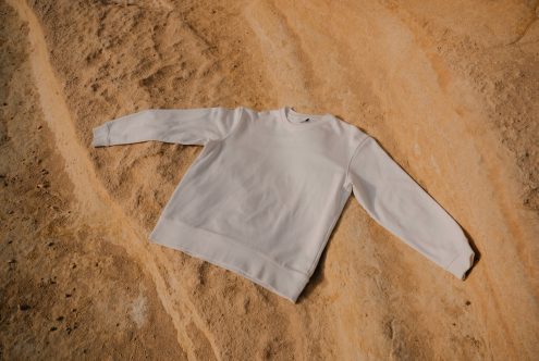 Blank cream sweatshirt laid flat showing back view on tan background