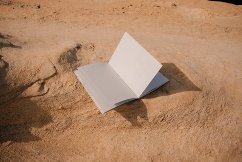 Open book mockup spread flat on desert sand with sharp shadows
